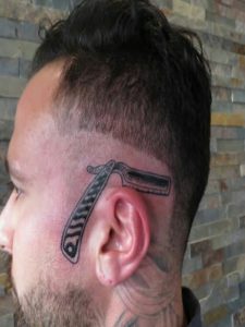 Man's face shows a straight razor tattoo in black ink near the ear; neck also covered in tattoos.