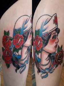 Thigh displays a vintage-style tattoo of a nurse wearing a cap with red roses and blue ribbons.