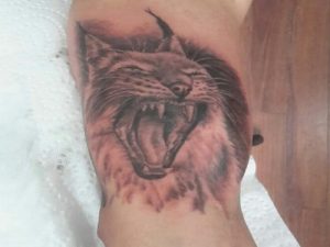 Forearm tattoo shows a roaring lynx with sharp white teeth, detailed fur and dark shading.