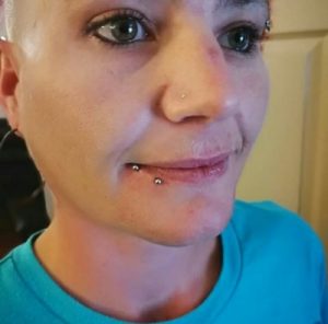 Woman with shaved head and facial piercings in her eyebrow, nose, and lip.