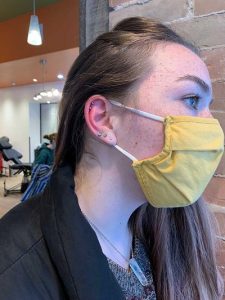 Woman with fresh ear piercings and a yellow face mask, showcasing cartilage and lobe jewelry.