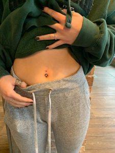 Person wearing gray sweatpants and a green hoodie with a navel piercing.