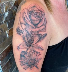 Shoulder tattoo featuring a rose, lily, and daisy in black and gray ink.