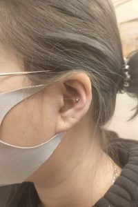 Close-up of a woman's ear with a tragus piercing and a gray face mask.
