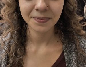 Close-up of a woman's face with curly hair and matching nose piercings on each side of her nose.