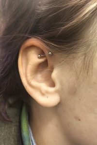 Ear shows a horizontal industrial piercing with a silver-colored barbell.