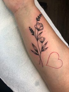 Arm displays a black ink tattoo of flowers along with a red outline of a heart shape.