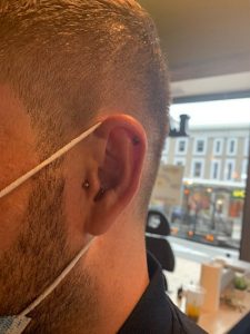 Man wears a face mask with three piercings in his ear.