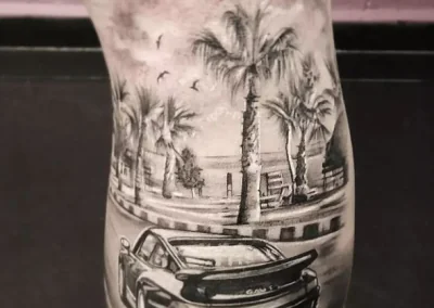Detailed black-and-gray tattoo shows a car with an 'EST-1979' license plate, palm trees, and birds in flight.