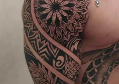 Shoulder and arm tattoo displays a mandala design, tribal patterns, and leaf elements in black ink.
