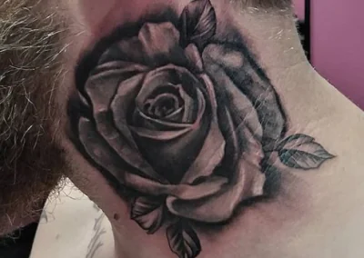 Black and gray rose tattoo with leaves decorates a man's neck, with a small '13' tattoo visible above the ear.