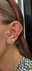 Ear shows multiple piercings with jewelry and a black ink tattoo.
