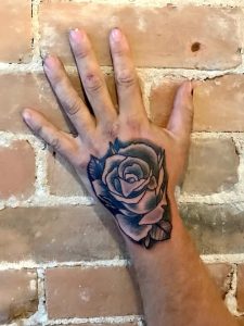 Hand with rose tattoo pressed against an exposed brick wall.
