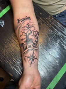 Forearm tattoo with tree, clock, compass, and names including Family, Noah, Mom, Dad, Colton, and Hyatt.
