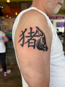 Tattoo of Chinese characters and a pig's head on a person's upper arm.