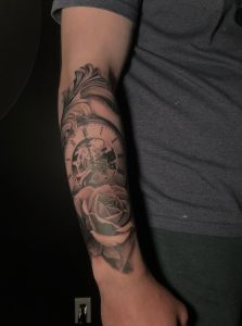 Forearm tattoo features a clock with visible gears and a rose in black and gray ink.