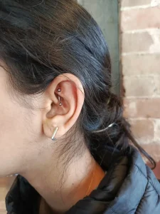Woman's ear displays a daith piercing with a curved barbell and a silver hoop earring.