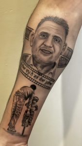 Arm tattoo featuring a portrait of a man with film strip detail and a smaller image of a man assisting a child on a bicycle.