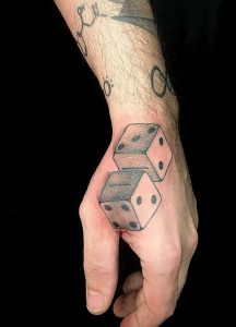 Dice tattoo on a hand shows two dice with black spots, displayed against a black background.