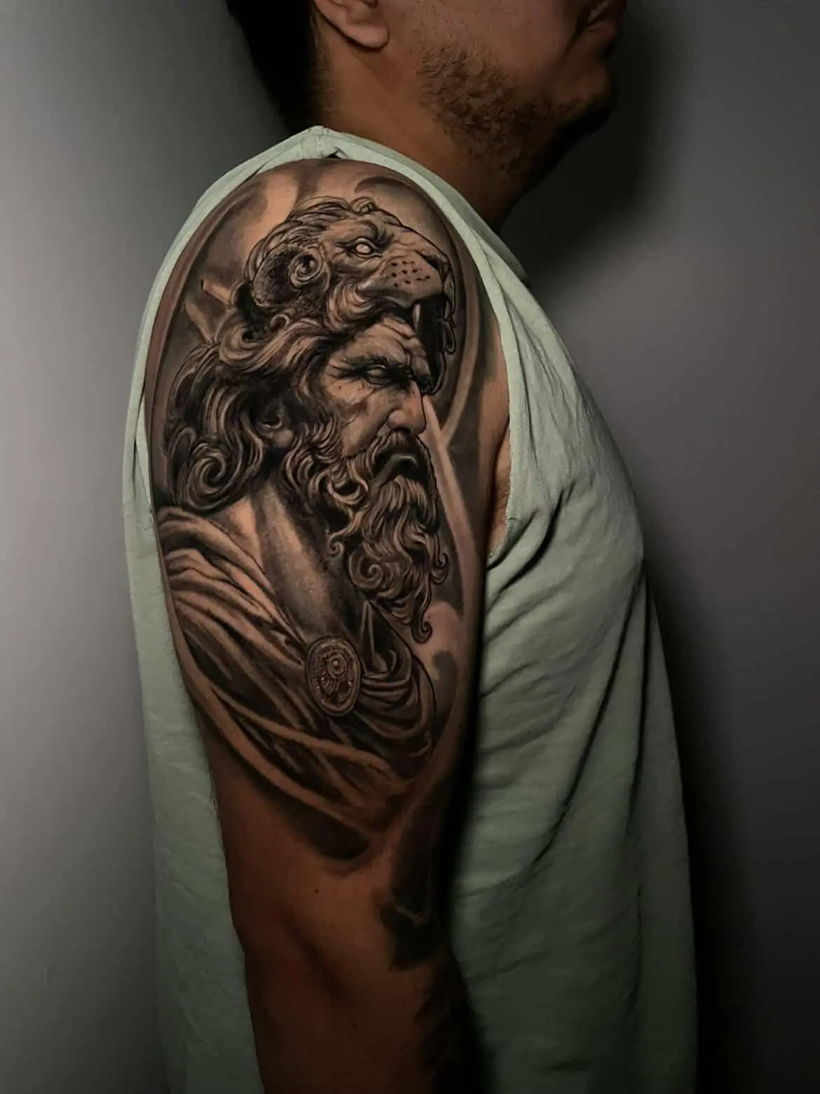 Man's arm displays a black and gray tattoo of Hercules wearing the Nemean lion skin.