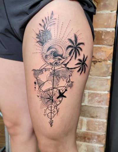 Tattoo on a thigh shows a world map, palm trees, compass, airplane, sun, and waves in black ink.