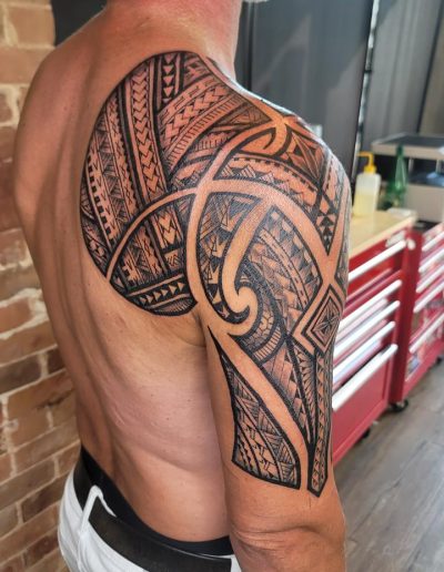 Man showcases a large, intricate black tribal tattoo design covering his shoulder and upper arm.