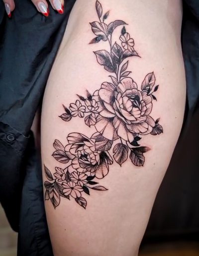Woman's thigh features a floral tattoo with roses and leaves in black ink.