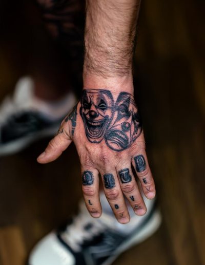 Tattooed hand displays clown faces and the word "LOVE" across the fingers.