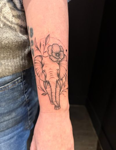 Elephant tattoo with flower on a person's forearm.