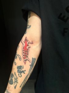 Tattooed arm shows a red anatomical rib cage and other tattoos including a devil and crossed swords.