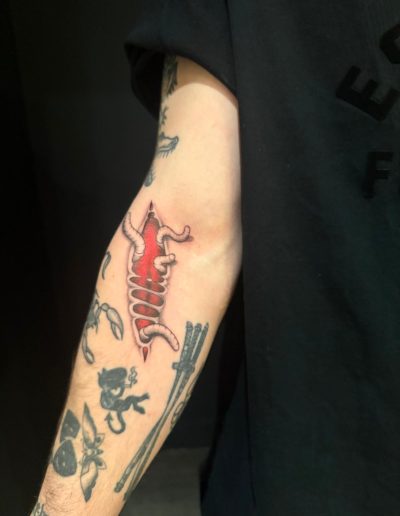 Tattooed arm shows a red anatomical rib cage and other tattoos including a devil and crossed swords.