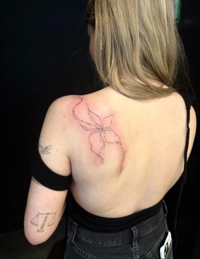 Woman shows a back tattoo of a flower outline, with a Libra scale and hummingbird tattoo on her left arm.