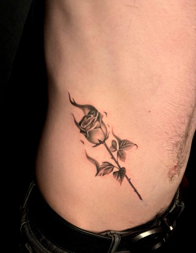 Black and grey tattoo of a rose on fire on a person's side
