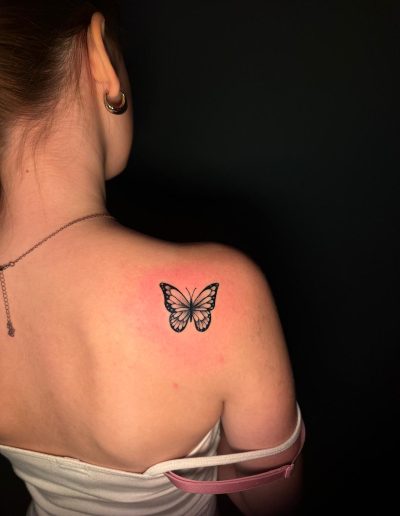Black butterfly tattoo on a woman's shoulder with pinkish skin