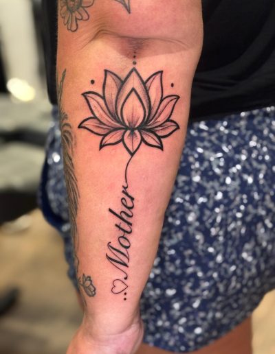 Close-up of a tattoo of a lotus flower with the word "Mother" written below it.