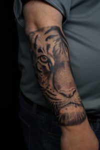Realistic black and grey tiger face tattoo on a man's arm