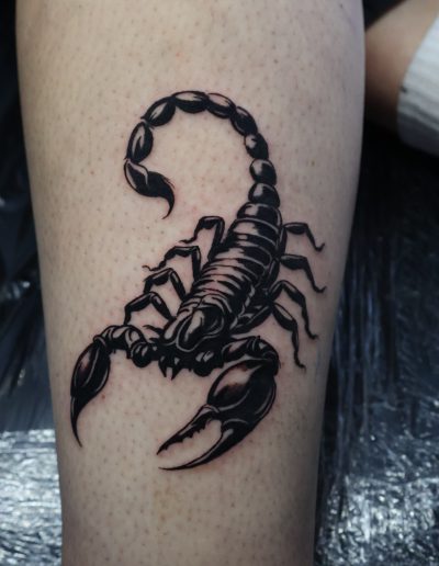 Black ink scorpion tattoo on a person's leg