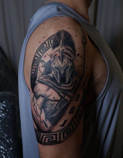 Spartan warrior tattoo on man's bicep, featuring intricate helmet and armor details.