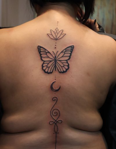 Back tattoo of a butterfly, lotus, moon, and unalome symbol