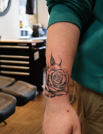 Black and gray rose tattoo on a person's forearm in a tattoo studio