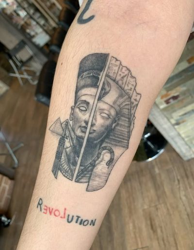Tattoo of Nefertiti bust split down the middle with "Revolution" below.