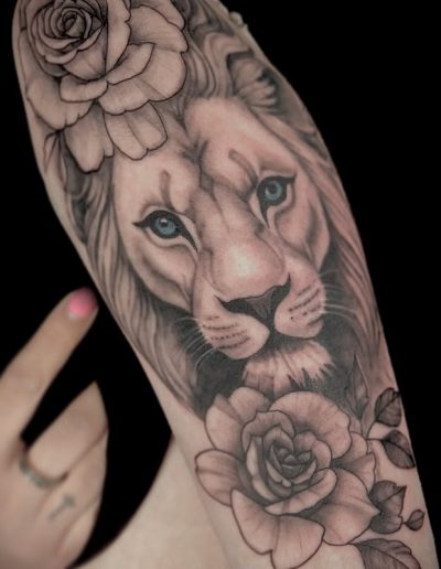 Detailed black and grey tattoo of a lion's face with blue eyes and roses