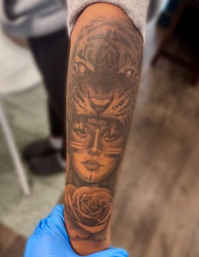 Tattoo of a tiger's face over a woman's face with a rose below.