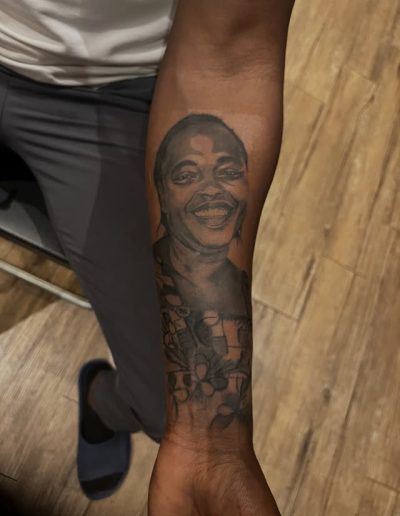 Tattoo of a smiling woman and flowers on a man's forearm.