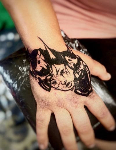 Close-up of a black ink tattoo of two Japanese oni masks on a person's hand.