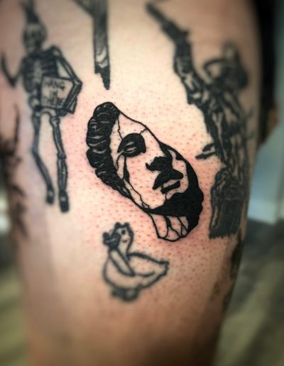 Close-up of a black ink tattoo of a skull mask and a duck