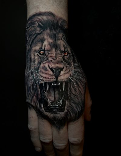 Realistic lion tattoo on hand, roaring with sharp teeth and glowing eyes.
