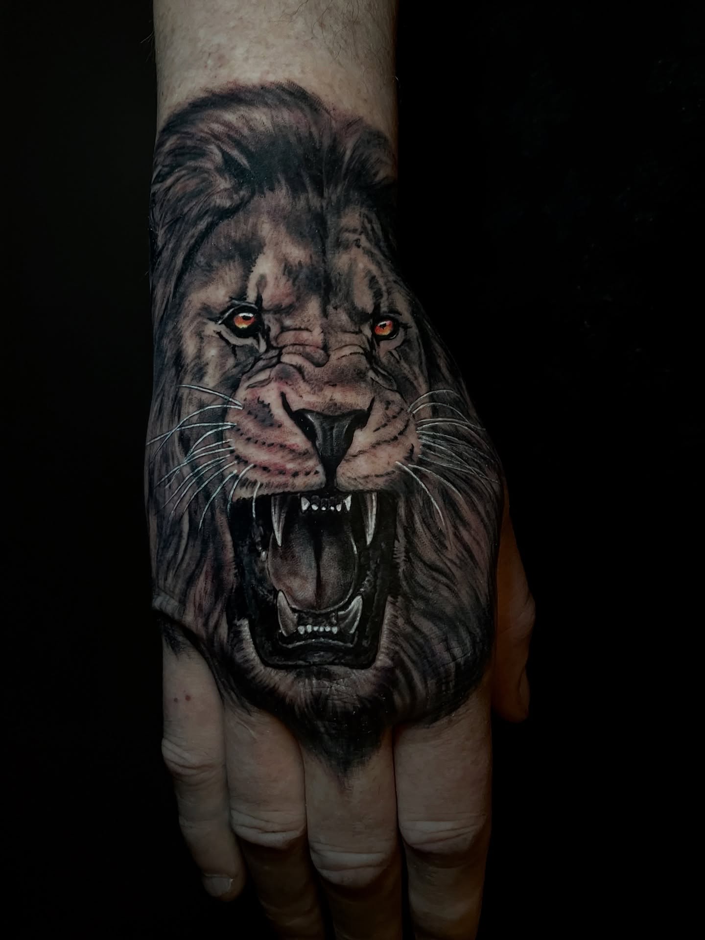Realistic lion tattoo on hand, roaring with sharp teeth and glowing eyes.