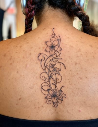 Close-up of a black ink floral tattoo with stars on a woman's upper back